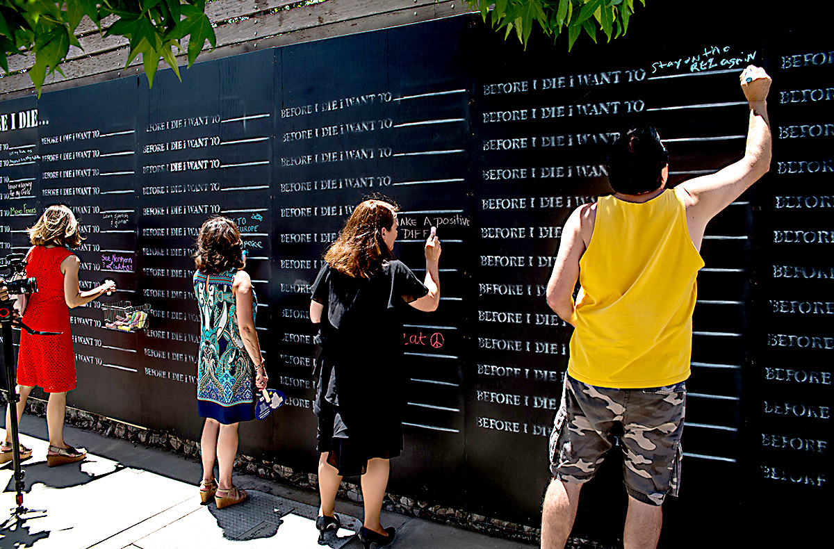 Individuals write their goals on the Before I Die Wall located in Coolidge Park.