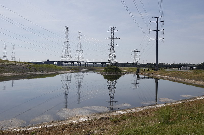 
              FILE - In this June 27, 2016, file photo, power lines tower over a coal ash pond from an abandoned coal fired power plant in Chesapeake, Va.  Environmental advocates are urging the Trump administration to reverse course on its move to set aside an Obama-era measure limiting water pollution from coal-fired power plants. (AP Photo/Steve Helber, File)
            