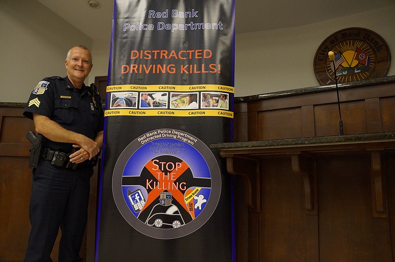Sgt. Rusty Aalberg stands next to the logo for Red Bank Police Department's new distracted driving prevention program. The logo was created by Red Bank High School student Mya Kennebrew, who won the design contest orchestrated by officers and the school's art teacher. Mya will be awarded with a plaque for her design work at an upcoming Red Bank Chamber of Commerce meeting. (Staff photo by Myron Madden)