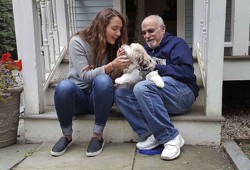 
              In this photo provided by the Boston Symphony Orchestra, Grace Ellrodt, left, and conductor David Zinman sit with Zinman's puppy Carlito outside his home Monday, Aug. 7, 2017, in Lenox, Mass. Ellrodt found the missing dog Sunday evening after hearing about a plea cellist Yo-Yo Ma made for help following the BSO's matinee concert at Tanglewood. (Hilary Scott/Boston Symphony Orchestra via AP)
            