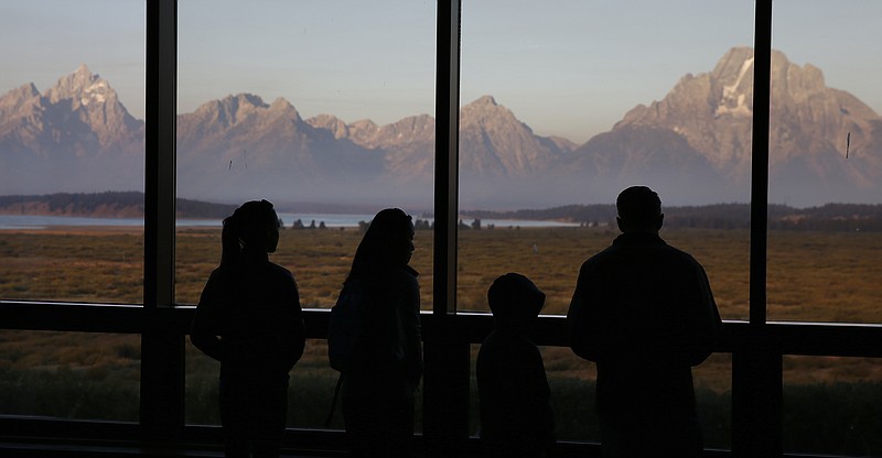 
              FILE- In this Aug. 28, 2016 file photo, visitors watch the morning sun illuminate the Grand Tetons, partially-obscured by smoke from nearby wildfires, as seen from within the Great Room at the Jackson Lake Lodge, in Grand Teton National Park, north of Jackson Hole, Wyo. Grand Teton National Park, normally in the shadow of the neighboring and world-renowned Yellowstone National Park in northwest Wyoming, is set to get its day in the sun with next week's total solar eclipse passing directly over the park. (AP Photo/Brennan Linsley, File)
            