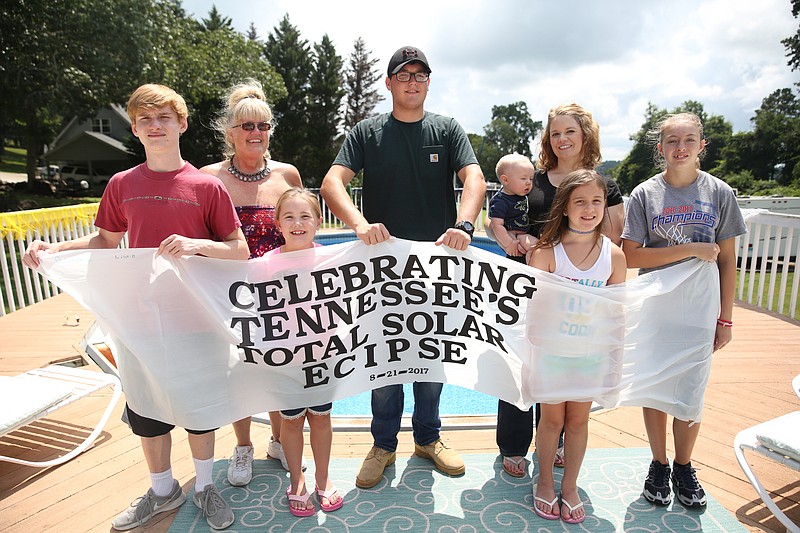 Hunter Esch, Jeanette Esch, Lila Higdon, Matthew Burkhart, Jaxon Roeser, Jeana Roeser, Aurora Esch and Gracie Roeser pose behind a banner created at the Jeanette's house Tuesday, Aug. 8, 2017, in Soddy-Daisy, Tenn. The family was working on several projects for their eclipse party, which include decorating a banner to go around the pool, art supplies for chalk drawings and stuffing treat bags.