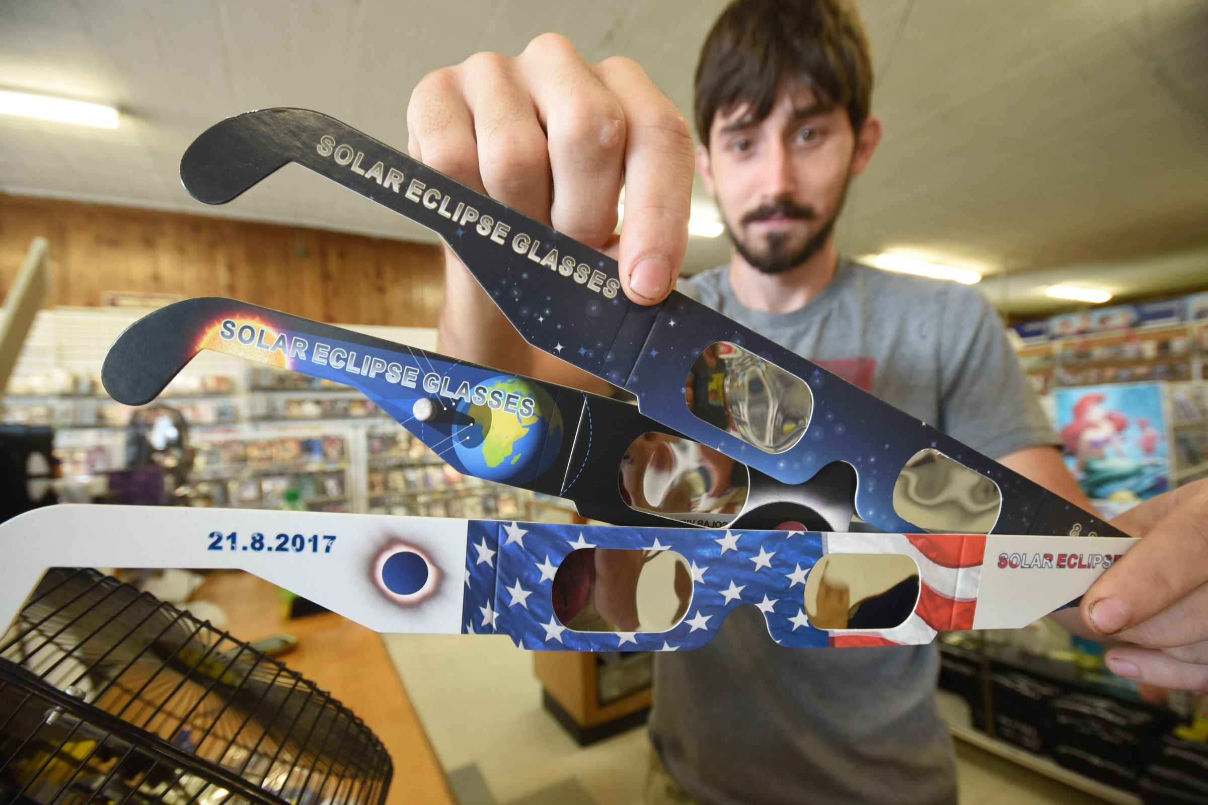 At the Movie Depot & Tanning store in Spring City, Tyler Whittaker holds the remaining types of cardboard eclipse glasses he has left on Friday. prepares for the Great American Total Eclipse.