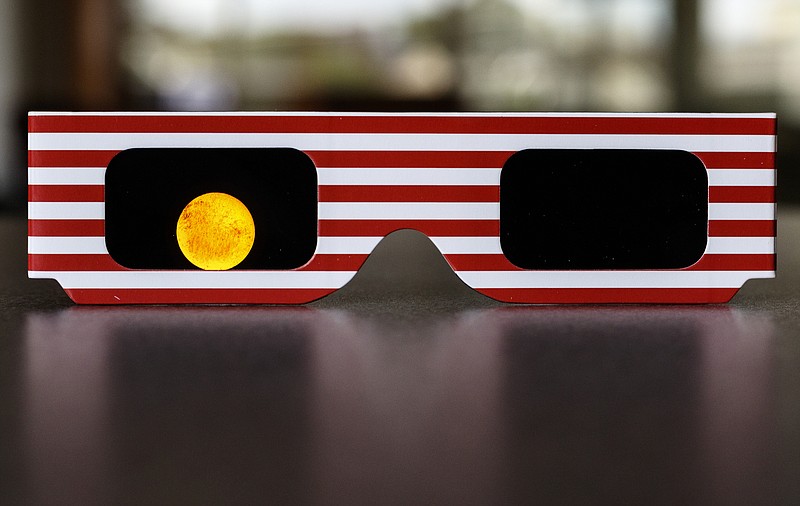 An LED flashlight is shined through a pair of ISO-certified eclipse glasses at full power to show how much light is blocked. It is unsafe to view a solar eclipse using any glasses but ISO certified eclipse viewing glasses.