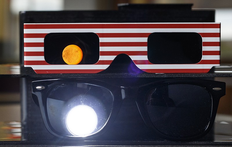 An LED flashlight is shone through a pair of ISO certified eclipse glasses, top, at full power while the same brand of flashlight is shined through a pair of regular sunglasses at its lowest power setting to demonstrate the difference in light transmission. It is unsafe to view a solar eclipse using anything but ISO certified eclipse viewing glasses.