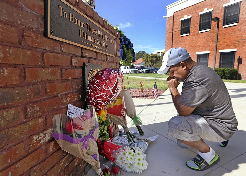After placing flowers at a makeshift memorial, Miguel Velez, say's a prayer for the officer that was killed on Saturday, Aug. 19, 2017 in Kissimmee, Fla. The Kissimmee Police Department says Sgt. Sam Howard died Saturday from his injuries. His colleague, Officer Matthew Baxter, died Friday night after the attack in a neighborhood of Kissimmee, located south of the theme park hub of Orlando. (Red Huber/Orlando Sentinel via AP)