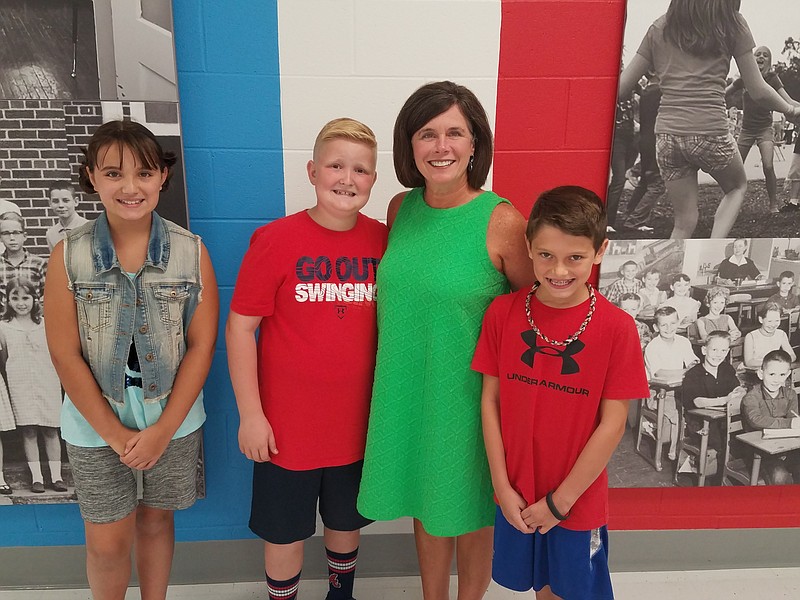 Shelby Putt, Preston Hendrix, Principal Allyson DeYoung and Owen Burk, from left, stand in front of the memorial wall for Falling Water Elementary located in Middle Valley Elementary School, which replaced both Falling Water and Ganns Elementary. Art and collages that celebrate the rich history of both former schools was an important part of the new building. (Staff photo by Shane Foley)