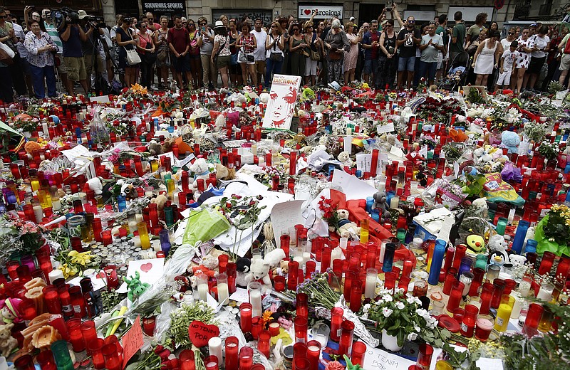 
              People stand next to candles and flowers placed on the ground after a terror attack that killed 14 people and wounded over 120 in Barcelona, Spain, Sunday, Aug. 20, 2017. (AP Photo/Manu Fernandez)
            