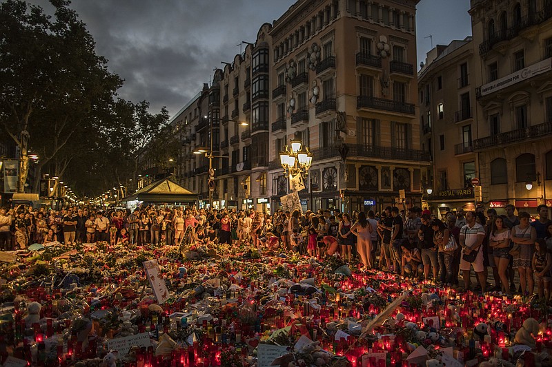 
              People stand next to candles and flowers placed on the ground, after a terror attack that left many killed and wounded in Barcelona, Spain, Monday, Aug. 21, 2017. The lone fugitive from the Spanish cell that killed 15 people in and near Barcelona was shot to death Monday after he flashed what turned out to be a fake suicide belt at two troopers who confronted him in a vineyard just outside the city he terrorized, authorities said. (AP Photo/Santi Palacios)
            