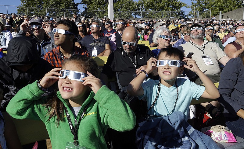 A crowd wears protective glasses as they watch the beginning of the solar eclipse from Salem, Ore., on Monday, Aug. 21.