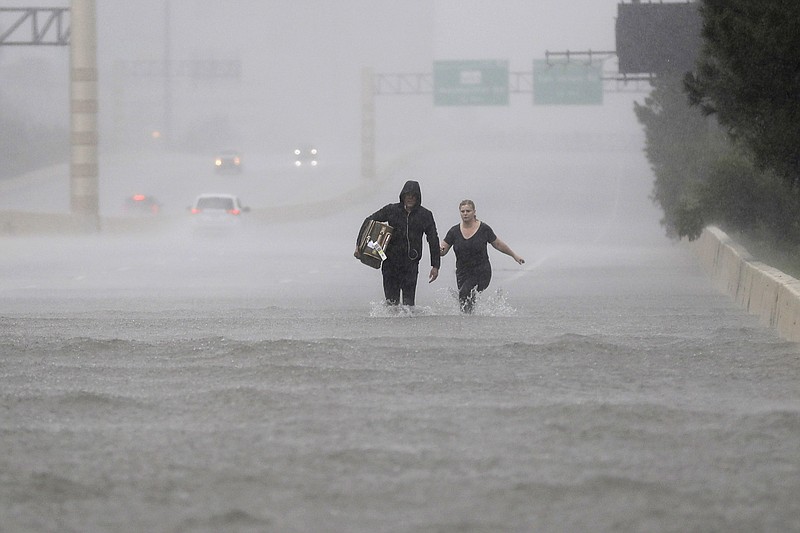 Two people walk down a flooded section of Interstate 610 in floodwaters from Tropical Storm Harvey on Sunday, Aug. 27, 2017, in Houston, Texas. (AP Photo/David J. Phillip)