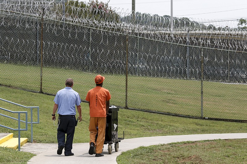 An inmate accompanied by a guard pushes a cart through the main exercise yard at Silverdale Correctional Facility.