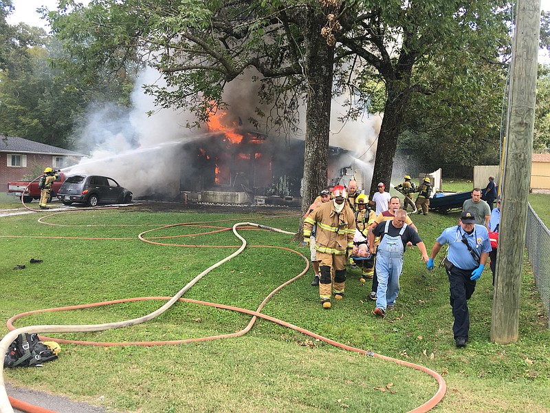 Firefighters work to get the blaze under control while off-duty Captain Steve Everett (in overalls, right front), Chattanooga firefighters, and some of the neighbors involved in the rescue help carry Charles Vaughn's wife on a stretcher to a waiting ambulance on Sunday, September 17, 2017.