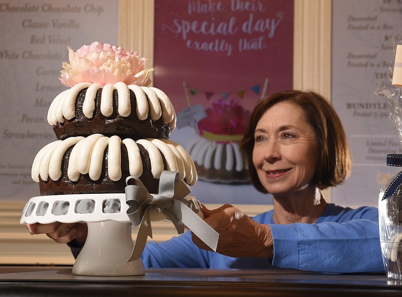 Melinda Mason, owner and operator of Nothing Bundt Cakes, displays a two-tiered Chocolate Chocolate Chip Bundt cake atop the center case at the store near Hamilton Place Mall. 
