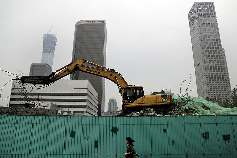 
              In this photo taken on Friday, Sept. 15, 2017, a woman walks by a machine demolish an old building at the Central Business District in Beijing. The Standard & Poor's rating agency cut China's credit rating on Thursday, Sept. 21, 2017 due to its rising debts, highlighting challenges faced by Communist leaders as they cope with slowing economic growth. (AP Photo/Andy Wong)
            