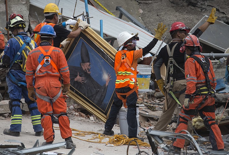
              Search and rescue workers remove a painting from a felled office building brought down by a 7.1-magnitude earthquake, as others raise their arms as a sign for people to maintain silence during their search for survivors in the Roma Norte neighborhood of Mexico City, Saturday, Sept. 23, 2017. As rescue operations stretched into day 5, residents throughout the capital have held out hope that dozens still missing might be found alive. (AP Photo/Moises Castillo)
            