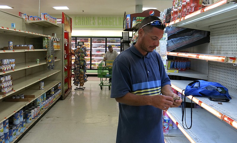 In this Monday, Sept. 25, 2017, photo, Christian Mendoza counts money in the aisle of a supermarket where he had hoped to buy bottled water but only found cans of juice, in San Juan, Puerto Rico. Mendoza said the car wash where he works hasn't re-opened so he has been selling bottled water, even though he isn't able to refrigerate it. (AP Photo/Ben Fox)