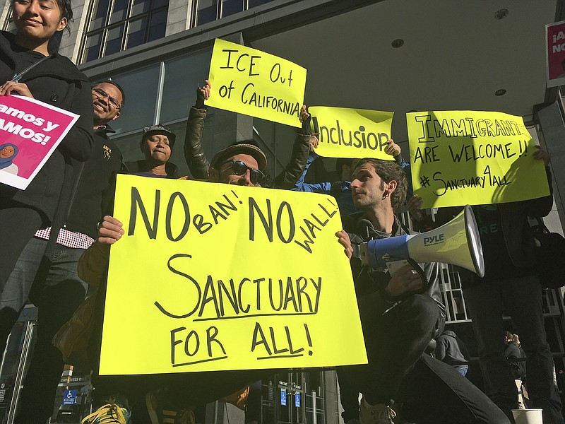 
              FILE - In this April 14, 2017, file photo, protesters hold up signs outside a courthouse where a federal judge will hear arguments in the first lawsuit challenging President Donald Trump's executive order to withhold funding from communities that limit cooperation with immigration authorities in San Francisco. Trump has unveiled a long list of immigration priorities he says must be included as part of any legislative package extending protections for young immigrants known as “Dreamers.” That includes increasing penalties against so-called “sanctuary cities” that refuse to cooperate and share information with federal immigration authorizes, including blocking them from receiving certain federal grants.  (AP Photo/Haven Daley, File)
            