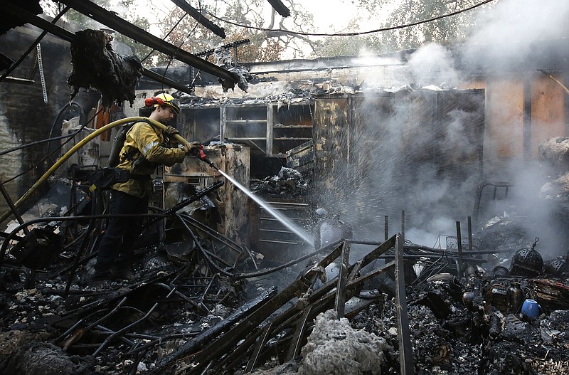 
              Firefighter Nick Gonzalez-Pomo, of the San Rafael Fire Department, waters down smoldering ashes on a garage Tuesday, Oct. 10, 2017, in Napa, Calif. Wildfires whipped by powerful winds swept through the California wine country sending thousands fleeing as flames rages unchecked through high-end resorts, grocery stores and tree-lined neighborhoods.(AP Photo/Rich Pedroncelli)
            