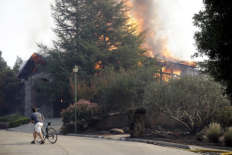 
              FILE - In this Oct. 9, 2017, file photo, a man walks next to a burning house in Silverado Crest subdivision in Napa, Calif. For many residents in the path of one of California's deadliest blazes, talk is of wind direction, evacuations and goodbyes. (AP Photo/Marcio Jose Sanchez, File)
            