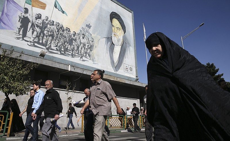 
              Iranian worshippers walk past a painting of the late revolutionary founder Ayatollah Khomeini and Basij paramilitary force members, at the conclusion of the Friday prayer ceremony, in Tehran, Iran, Friday, Oct. 13, 2017. (AP Photo/Vahid Salemi)
            
