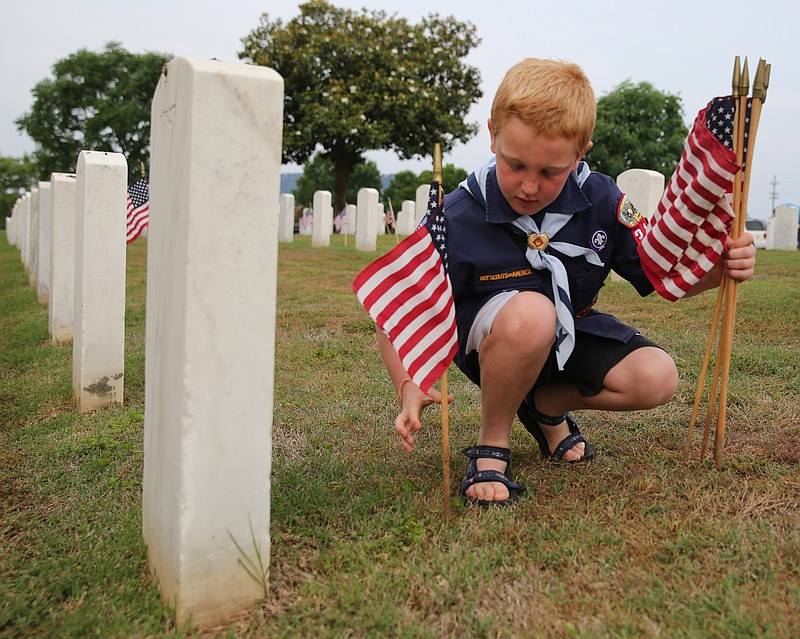 A Cub Scout places a flag in front of a gravestone at the Chattanooga National Cemetery in 2014 as part of an annual event by the Cherokee Area Council, Boy Scouts of America.