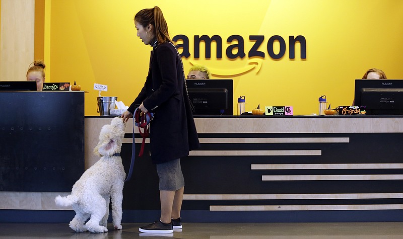FILE - In this Wednesday, Oct. 11, 2017, file photo, an Amazon employee gives her dog a biscuit as the pair head into a company building, where dogs are welcome, in Seattle. Amazon says it received 238 proposals from cities and regions hoping to be the home of the company's second headquarters. The online retailer kicked off its hunt for a second headquarters in September, promising to bring 50,000 new jobs. It will announce a decision sometime in 2018. (AP Photo/Elaine Thompson, File)