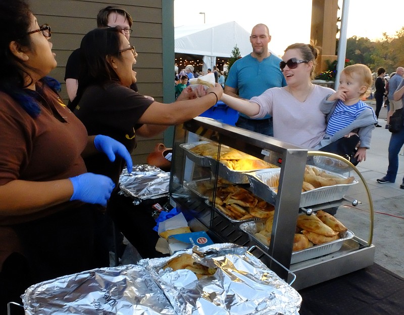 Kristina Mason holds her daughter Sasha, 13 mos., as she purchases an Empanada from Keila Lazeano, second from left, and Sakei Riggs at The Commons grand opening in Collegedale. Customer Mike Chaigne, back center, waits his turn to purchase from the vendor, Aji Peruvian Restaurant of Ooltewah.