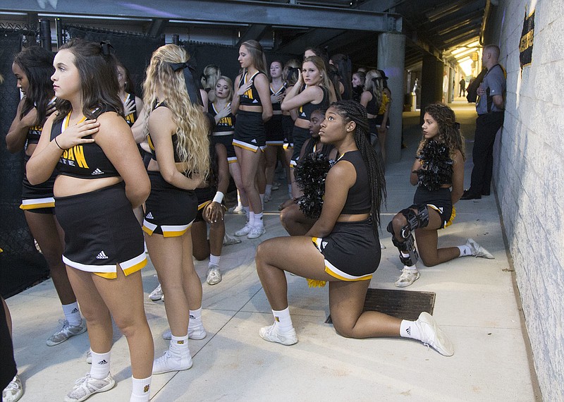 In this Saturday, Oct. 21, 2017, file photo, Four of the five Kennesaw State cheerleaders who took a knee three weeks ago during the Kennesaw State football game, take a knee once again out of sight of the fans under the visitors' bleachers, during the national anthem before an NCAA college football game between Kennesaw State and Gardner-Webb in Kennesaw, Ga. Kennesaw State, which moved its football cheerleaders inside a stadium tunnel after a group of black cheer squad members knelt during the national anthem, has decided to let them again take the field during pre-game ceremonies. (Kelly J. Huff/The Marietta Daily Journal via AP, File)