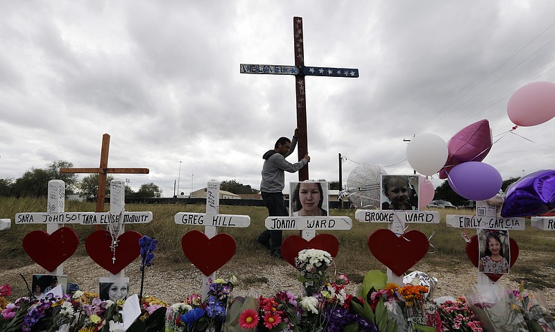 Miguel Zamora stands a cross for the victims of the Sutherland Springs First Baptist Church shooting at a makeshift memorial, Saturday, Nov. 11, 2017, in Sutherland Springs, Texas. A man opened fire inside the church in the small South Texas community on Sunday, killing more than two dozen. Zamora carried the cross for three days to reach the site. (AP Photo/Eric Gay)