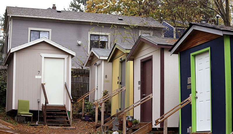 In this photo taken Thursday, Nov. 9, 2017, a row of tiny houses at a homeless encampment stand in view of a full-size home behind, in Seattle. Tiny homes could be the solution to all kinds of housing needs, offering warmth and security for the homeless, an affordable option for expensive big cities and simplicity for people who want to declutter their lives. However, that seemingly broad support fails to translate into acceptance when tiny home developers try to build next door. (AP Photo/Elaine Thompson)