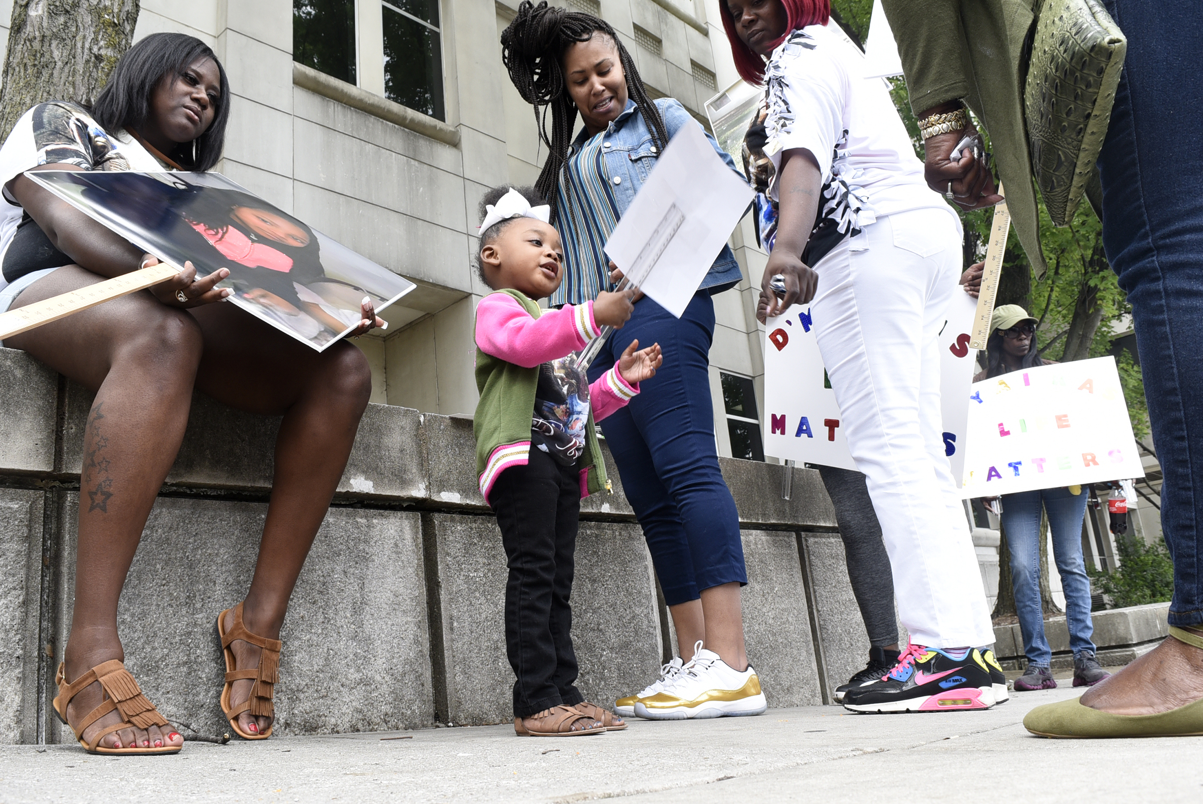Two-year old Layla Martin looks at the sign that she is to carry. A march was held downtownon May 25, 2017 to remember the victims of the Woodmore Bus Crash and draw attention to Durham Transportation being retained as the contractor for the county's buses.