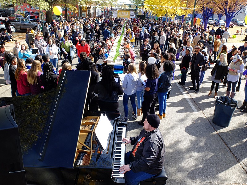 Hamilton County Department of Education employee John Demerdjian, bottom center, plays piano for the CSAS Choir as hundreds enjoy eating Monday, Nov. 20, in the middle of M.L. King Boulevard for Causeway's annual citywide Thanksgiving dinner. The event is called 1TABLE, and volunteers serve free food just two blocks from last years site, now in front of the Bessie Smith Cultural Center.