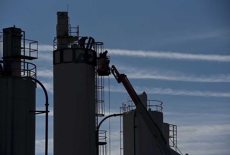 A small crew of men work vertically near the top of a storage tank at the American Colloid Mineral Co. plant at 3406 Alton Park Blvd. in South Chattanooga  as aircraft vapor trails create a horizontal backdrop in frigid temperatures.