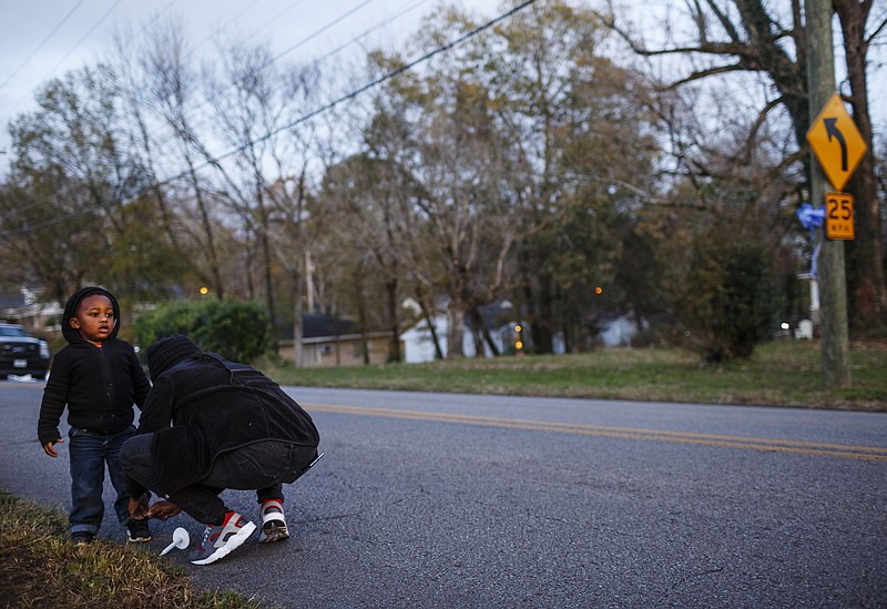 Beverly Lockett ties Kyrie Cox's shoe near the spot where Hamilton County school bus 366 came to rest while on their way to a community vigil to remember victims of last year's bus crash on Talley Road on Tuesday, Nov. 21, 2017, in Chattanooga, Tenn. Parents, friends, and supporters gathered near the spot where one year ago Tuesday, six children from Woodmore Elementary School were killed after bus 366 overturned on the residential street.