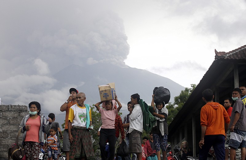 Villagers carry their belongings during an evacuation following the eruption of Mount Agung, seen in the background, in Karangasem, Indonesia, Sunday, Nov. 26, 2017. The volcano on the Indonesian island of Bali has rumbled into life with a series of eruptions that temporarily disrupted some international flights to the popular tourist destination and dusted nearby resorts and villages with a thin layer of ash. (AP Photo/Firdia Lisnawati)