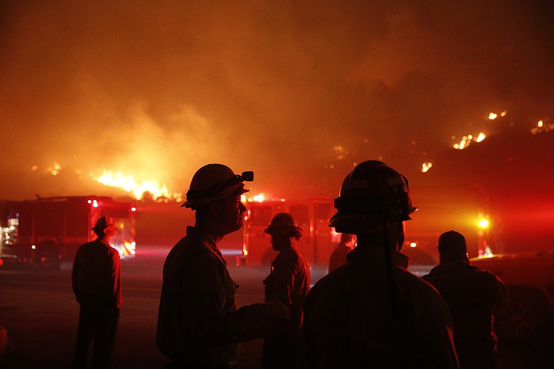 Firefighters gather in front of a residential area as a wildfire burns along the 101 Freeway Tuesday, Dec. 5, 2017, in Ventura, Calif. Raked by ferocious Santa Ana winds, explosive wildfires northwest of Los Angeles and in the city's foothills burned a psychiatric hospital and scores of homes and other structures Tuesday and forced the evacuation of tens of thousands of people. (AP Photo/Jae C. Hong)