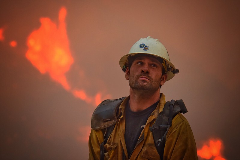 In this photo provided by the Santa Barbara County Fire Department, county fire hand crew member Nikolas Abele keeps an eye on a hillside for any stray embers during a firing operation in Santa Monica Canyon in Carpinteria, Calif., Monday, Dec. 11, 2017. Ash fell like snow and heavy smoke had residents gasping for air Monday as a wildfire exploded in size, becoming the fifth largest in state history. (Mike Eliason/Santa Barbara County Fire Department via AP)