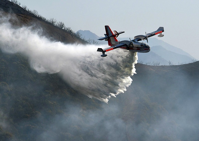 In this photo provided by the Santa Barbara County Fire Department, a Bombardier 415 Super Scooper makes a water drop on hot spots along the hillside east of Gibraltar Road in Santa Barbara, Calif., Sunday morning, Dec. 17, 2017. One of the largest wildfires in California history is now 40 percent contained but flames still threaten coastal communities as dry, gusty winds are predicted to continue. (Mike Eliason/Santa Barbara County Fire Department via AP)