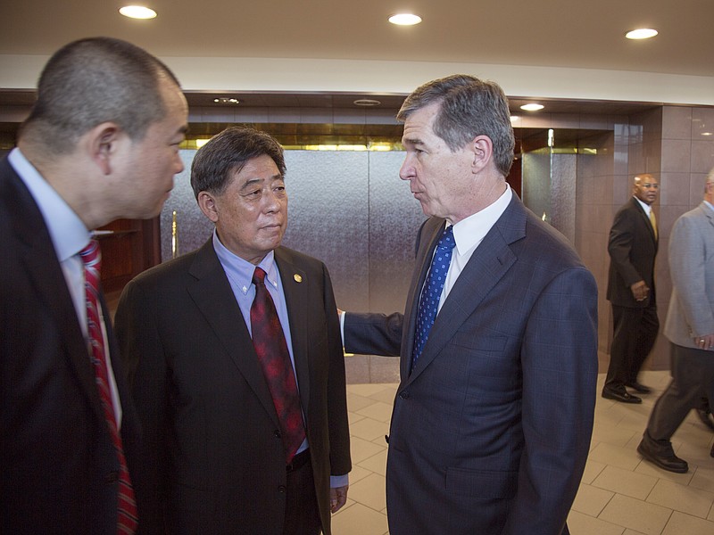 In a photo provided by the North Carolina Governors Office, North Carolina Gov. Roy Cooper, right, speaks to Triangle Tire Chairman Ding Yuhua, center, and his translator Tuesday, Dec. 19, 2017, at Edgecombe Community College in Tarboro, N.C., after the company announced plans to build a tire plant that would eventually employ 800 workers and produce 6 million tires a year. (North Carolina Governors Office via AP)