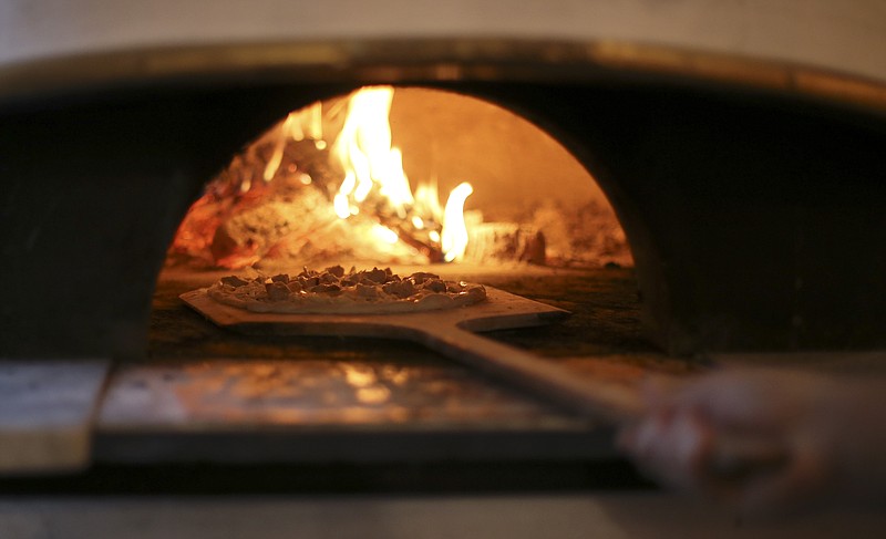 Owner Justin Bennett puts a Sweet Thai Chicken pizza in the oven for his wife at Pizzeria Cortile on Wednesday, Dec. 20, 2017 in Chattanooga, Tenn. According to the menu, the Sweet Thai Chicken pizza has "peanut sauce, cheese blend, roasted chicken, embered onions, cilantro and green onion."