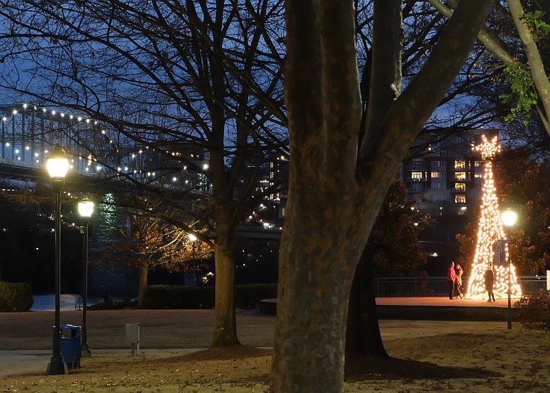 A couple has their photo taken by the lighted tree at Coolidge Park on a recent evening. Holiday lights will continue to glow around Chattanooga until New Year's day.