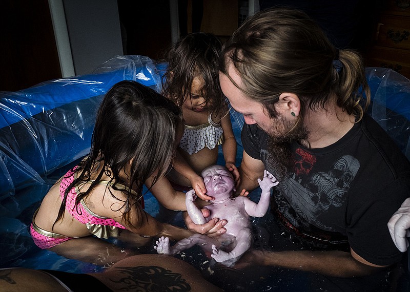 Dan, Stella, left, and Willow cradle Staxon in the moment following his birth. Both girls helped their father to deliver the baby, while midwife Carolyn waited on hand to intervene in any emergency.