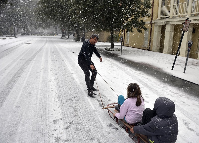 Ramon Martinez takes advantage of little car traffic to pull a sleigh filled with his children Amy and Anthony down Bull Street toward Monterey Square, in Savannah, Ga. Wednesday, Jan. 3, 2018. Snow started falling late Wednesday morning in the Savannah area shutting down the city. (Steve Bisson/Savannah Morning News via AP)