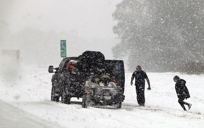 People attend to their vehicle on Interstate 26, near Savannah, Ga., Wednesday, Jan. 3, 2018. A brutal winter storm dumped snow in Tallahassee, Fla., on Wednesday for the first time in nearly three decades before slogging up the Atlantic coast and smacking Southern cities such as Savannah and Charleston, South Carolina, with a rare blast of snow and ice. (AP Photo/Robert Ray)