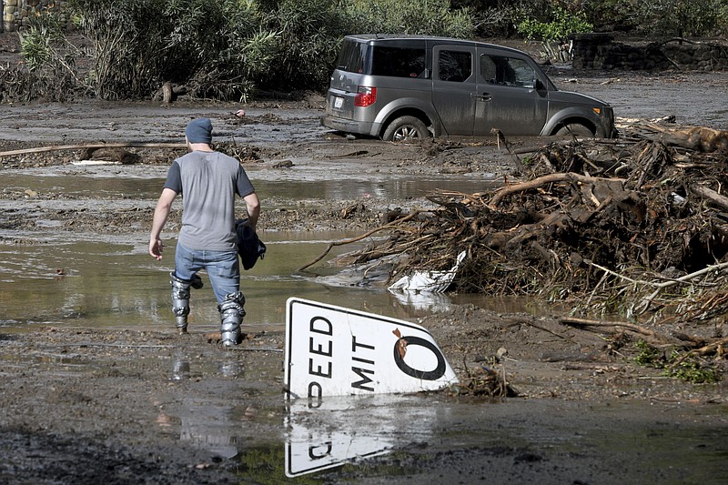 Mitchell Barrett crosses mud from an overflown creek on Sheffield Drive in Montecito, Calif., following the heavy rain, Tuesday, Jan. 9, 2018. Barrett was going to check on his parents' house in Montecito. (AP Photo/Michael Owen Baker)