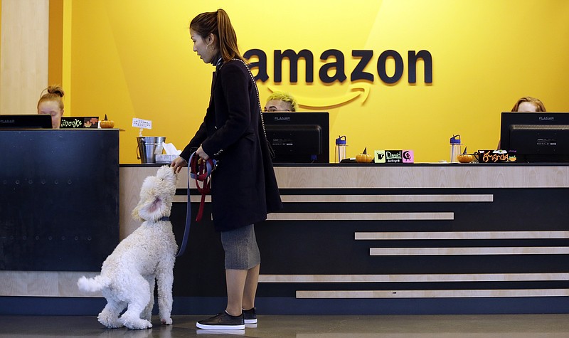 FILE - In this Wednesday, Oct. 11, 2017, file photo, an Amazon employee gives her dog a biscuit as the pair head into a company building, where dogs are welcome, in Seattle. Amazon announced Thursday, Jan. 18, 2018, that it has narrowed its hunt for a second headquarters to 20 locations, concentrated among cities in the U.S. East and Midwest. Toronto made the list as well, keeping the company’s international options open. (AP Photo/Elaine Thompson, File)