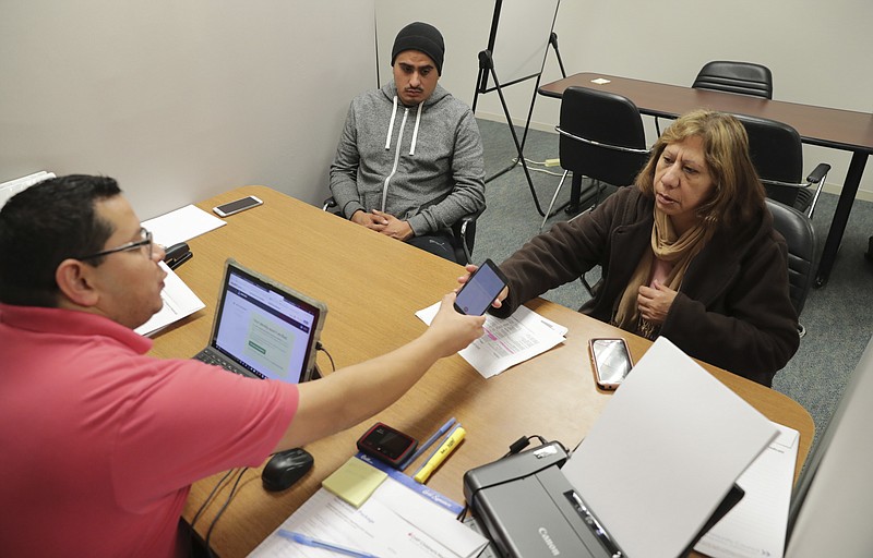In this Dec. 27, 2017, photo, Community Council health care navigator Fidel Castro Hernandez, left, hands a Spanish help line phone to legal U.S. resident Maria Ana Pina, right, as she signs up for the Affordable Care Act with her son Roberto Pina at the Community Council offices in Dallas. Since President Donald Trump took office a year ago, the number of Latino immigrants accessing public health services and enrolling in federally subsidized insurance plans has dipped substantially, according to health advocates across the country. (AP Photo/LM Otero)