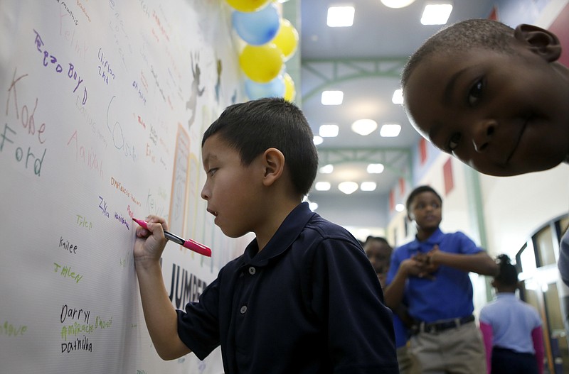 As fellow first-grader Keely Derrick looks at the camera, Pedro Andres-Pascual signs his name on the "I Jumped a Level" banner at Orchard Knob Elementary School on Wednesday, Jan. 24, 2018 in Chattanooga, Tenn. Students' reading success was celebrated with stickers and the chance to sign the banner.