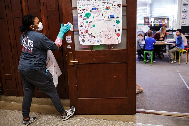 Parent volunteer Nichole Newson wipes down a doorway as students are in class during a group effort to sanitize surfaces at Chattanooga School for the Arts and Sciences on Tuesday, Jan. 30, 2018, in Chattanooga, Tenn. As the country grapples with one of the worst flu seasons in years, schools are working to combat the spread of the disease.